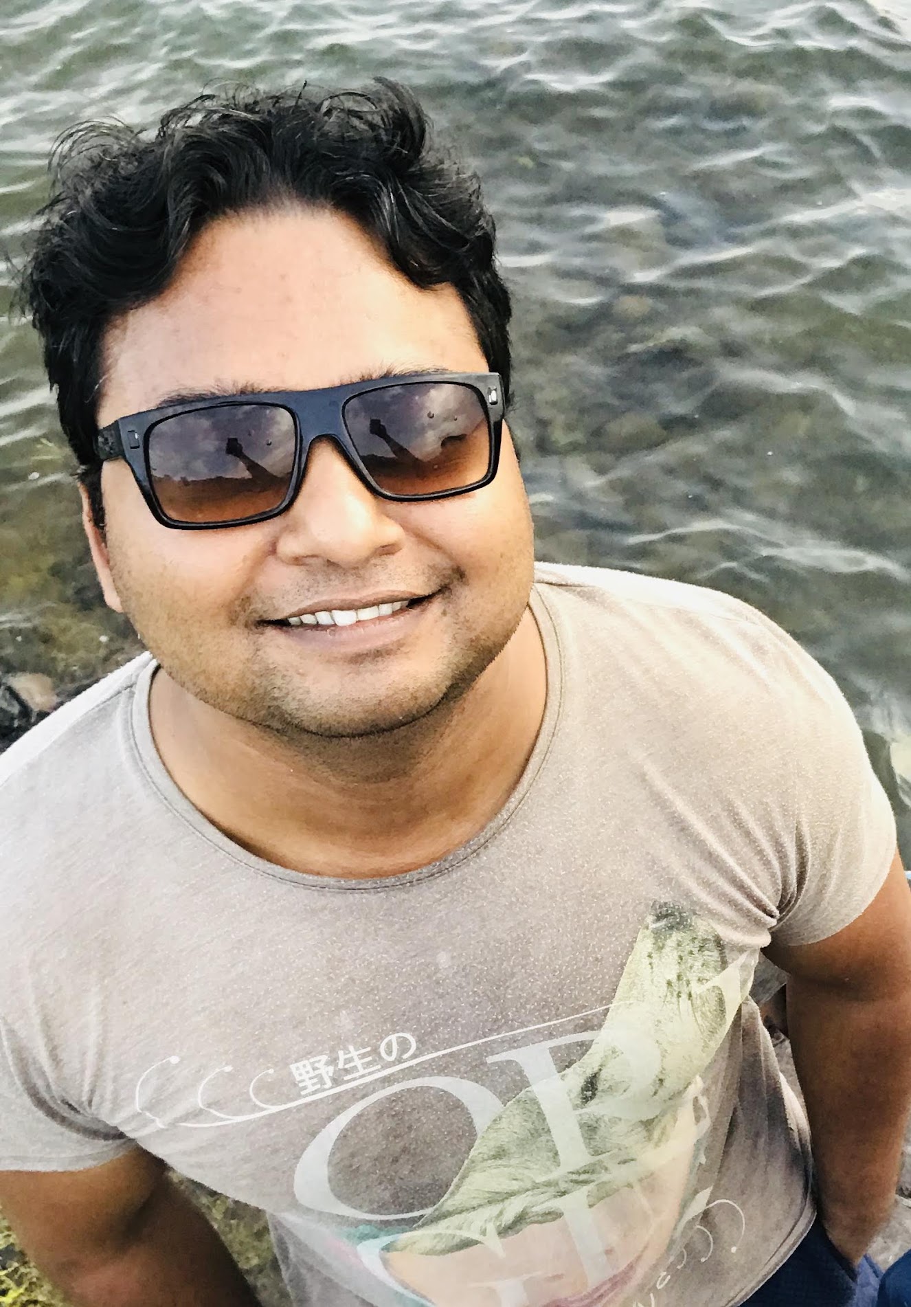 Suchay smiling beside the water in sunglasses